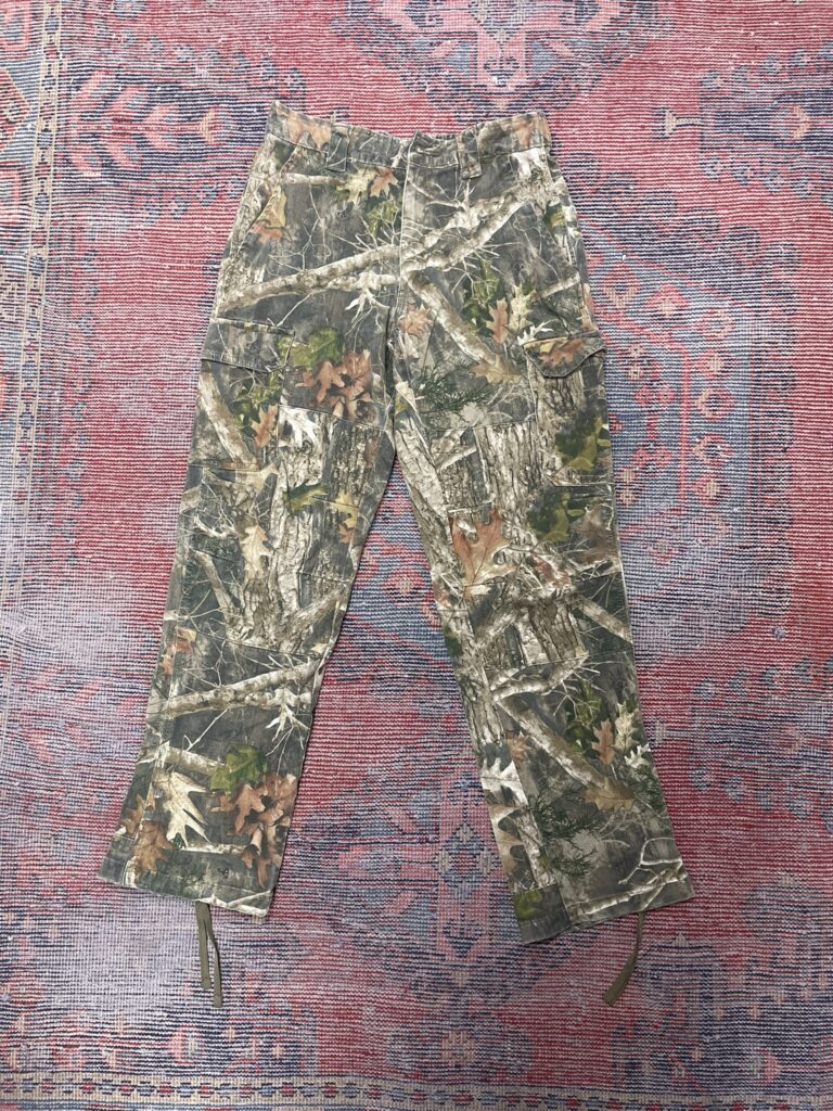Forest camo pants with straight-leg cut, laid on tribal rug